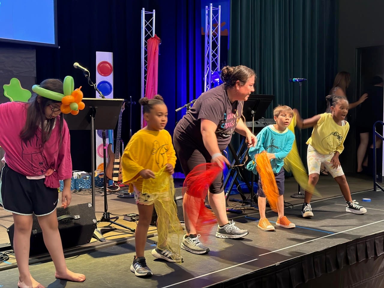Miss Bri leading children in a Zumbini Dance Party on stage with colorful scarves