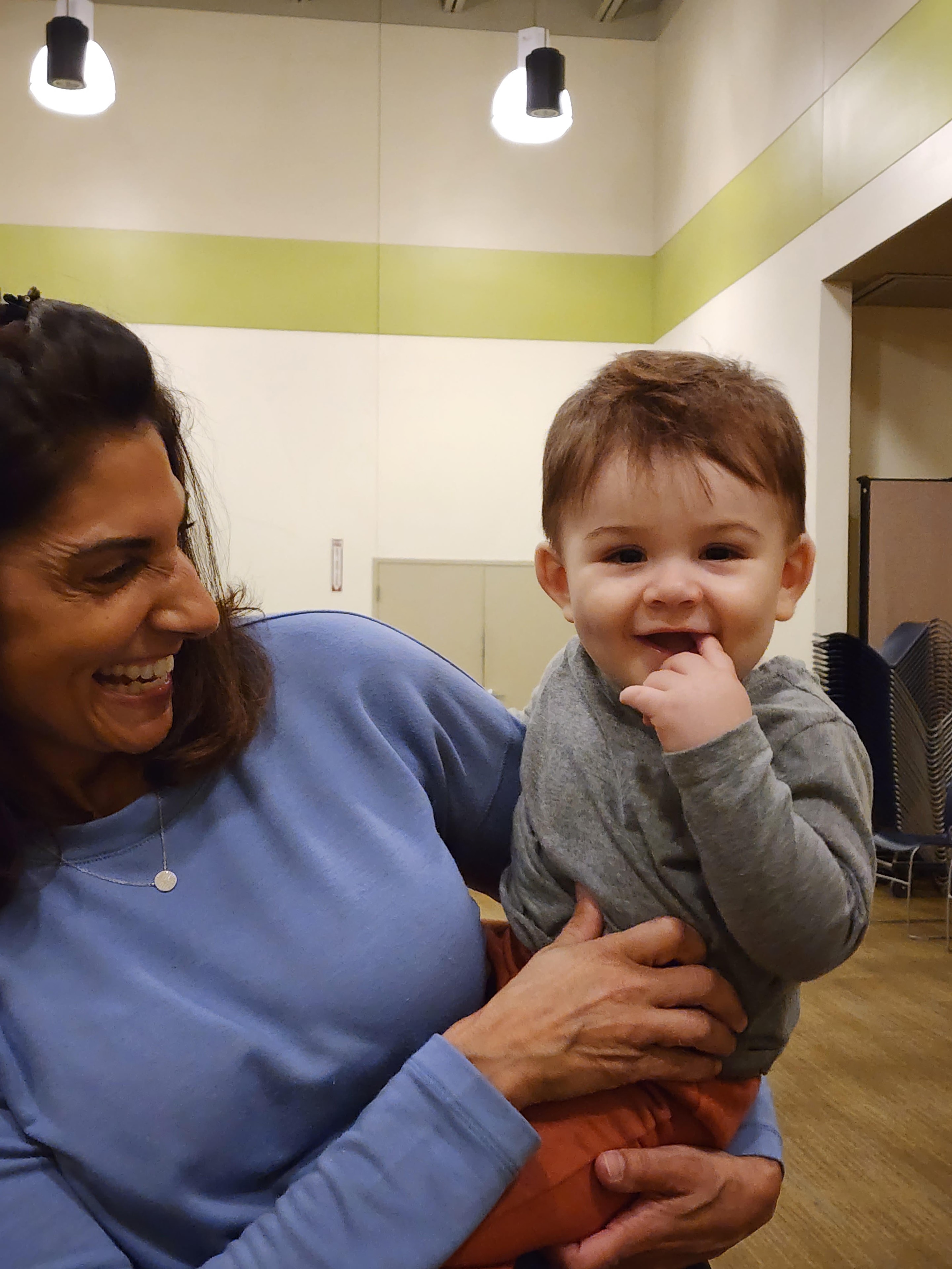 A woman laughing while holding a smiling baby during a Zumbini class