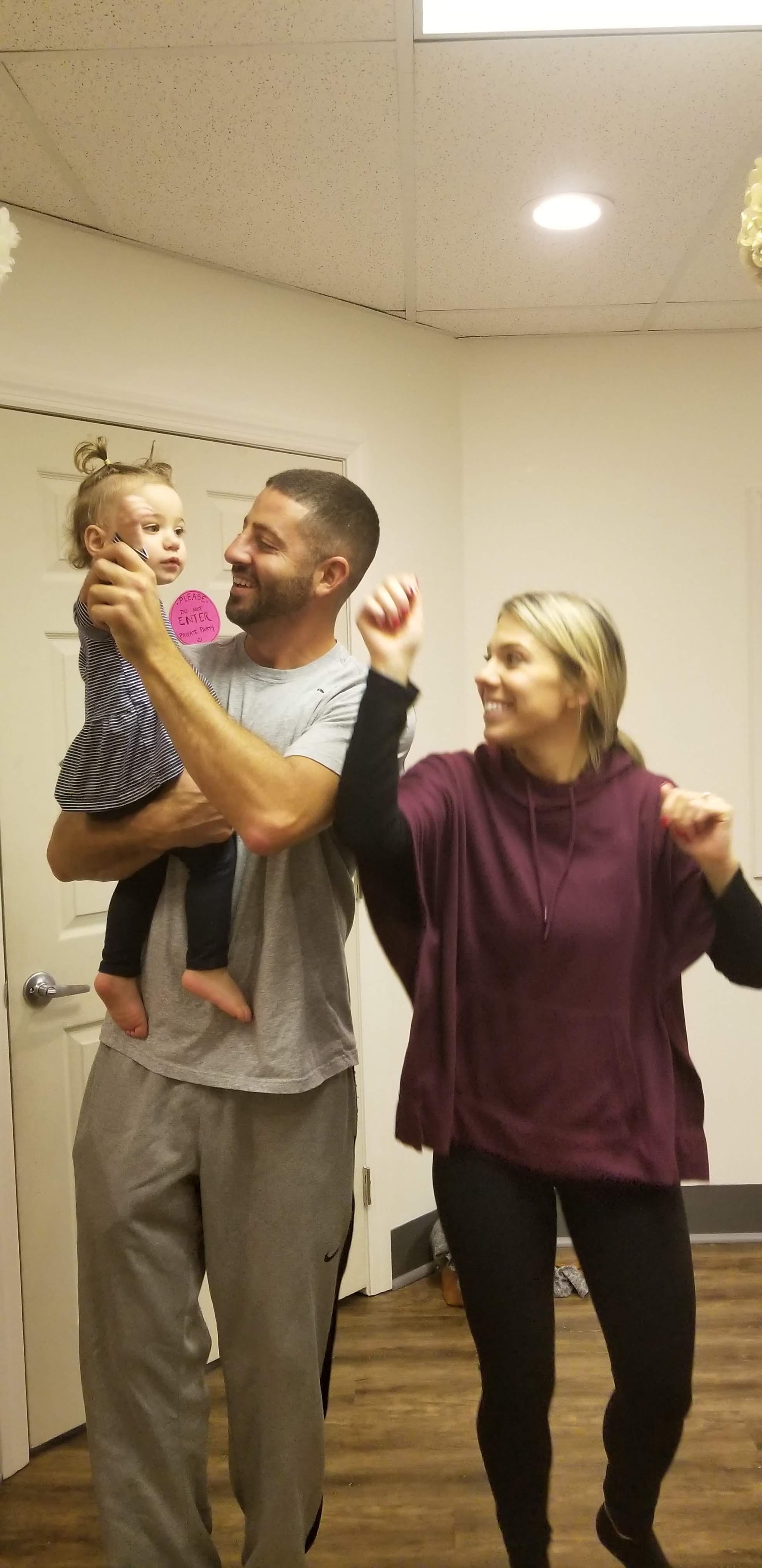A dad holding his toddler while a mom dances joyfully beside them during a Zumbini class